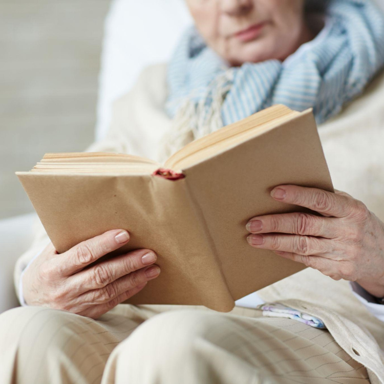 Mulher sentada num cadeirão a segurar um livro aberto com ambas as mãos enquanto lê.